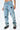 Pantalon Beleo Bleu Jean porté par une mannequin femme, vue de trois quarts du bas, fleurs de lys noires sur denim clair