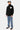 Pull Emile Noir à col montant porté de profil en pied par un homme, avec jean à motifs bleus et casquette