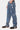 Pantalon Flex Bleu Jean porté de profil par un mannequin homme, fleurs de lys bleues et blanches sur la jambe, baskets noires