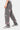 Pantalon Flex Gris porté de profil par un mannequin homme, fleurs de lys roses et blanches sur la jambe, baskets grises