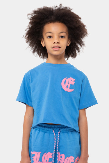 T-shirt Jasnova Bleu court porté par un enfant, de face, grande lettre rose gothique brodée sur la poitrine