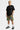 Short cargo Jolan Kaki porté de trois quarts par un mannequin homme blond, t-shirt noir et baskets noires