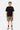 T-shirt Juicy Noir porté en pied par un mannequin homme avec short cargo kaki, chaussettes noires et baskets