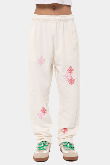 Jogging Jatacha Écru porté de face par un enfant, fleurs de lys roses brodées sur les jambes, baskets blanches et vertes