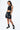 Short Maestro Noir porté par une mannequin femme avec top noir, main dans la poche, broderie pyramide et cordons tressés