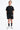 T-shirt Naava Noir porté par un garçon avec short noir assorti, de face en pied, chaussettes noires