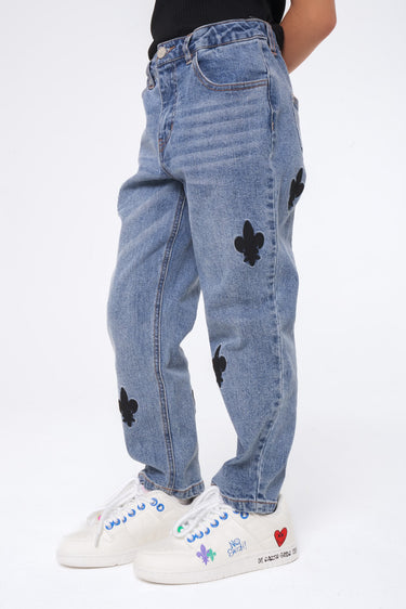 Jean Neleo Bleu jean porté par un enfant, détail des patchs fleur de lys noirs sur la jambe, baskets blanches