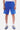Short Ninon Bleu porté par un homme, de face à mi-cuisse, fleurs de lys brodées, baskets bleues et chaussettes blanches