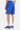 Short Ninon Bleu vu de dos et de côté, porté par un homme, fleur de lys brodée, baskets bleues à smiley