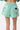 Short Jazeon Vert à rayures blanches vu de dos porté, étiquette noire, poches et écussons papillon et arc-en-ciel