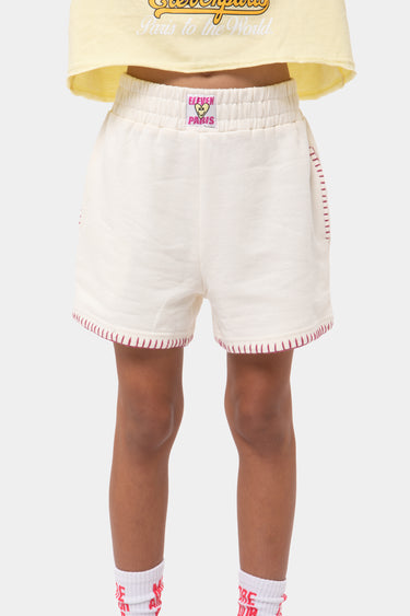 Short Poitier Écru en molleton, plan de face à la taille, étiquette Eleven Paris rose et surpiqûres rouges contrastées