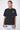 T-shirt Saule Noir Délavé porté par un mannequin femme, de face, cœurs sur la poitrine, jogging gris à fleurs Eleven Paris