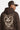 Sweat à capuche Tevy Marron porté par un homme, de dos, casquette trucker, cœur écru et graffiti Vandals Gone Over Peace