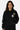 Sweat à capuche Toncho Noir porté de face par une femme, fleurs de lys kaki et blanche sur la poitrine