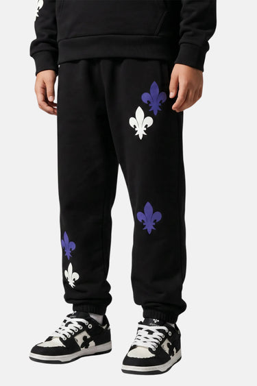 Jogging Tutti Noir en gros plan porté de trois quarts, fleurs de lys blanches et violettes sur la jambe et baskets