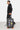 Valise Fugers Gris Foncé S tenue par un homme en sweat et jogging noirs, patchs colorés, roulettes orange