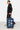 Valise Fugers Bleu Marine S tenue par un homme en sweat et jogging noirs, patchs colorés, roulettes orange