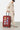 Valise Fugers Rouge M tenue par un homme en casquette et sweat jogging beige, patchs colorés, roulettes orange