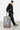 Valise Fugers Argent M tenue par un homme en casquette et sweat jogging noirs, patchs colorés, roulettes orange