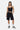 Short Ninon Noir ample porté par une femme avec brassière noire, de face en pied, main dans la poche, baskets grises