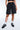 Short Ninon Noir délavé porté par une femme, de face, cordon gris et poche, baskets noires et chaussettes blanches