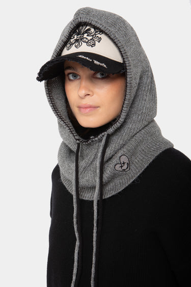Accessoire Fanette Gris, cagoule en maille grise portée avec une casquette, cordon de serrage et cœur brodé