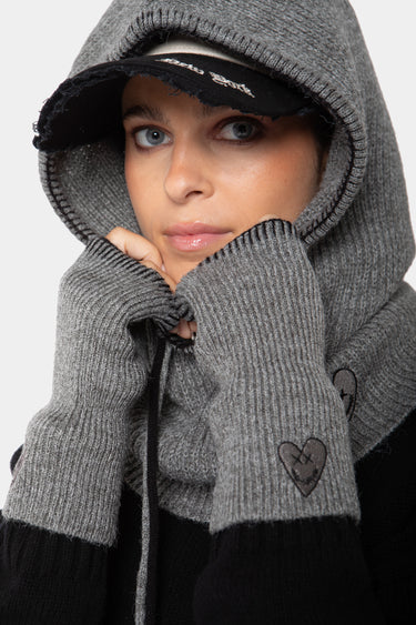 Cagoule et mitaines en maille Fraise Gris portées par une femme avec casquette noire, coeur noir brodé sur le gant
