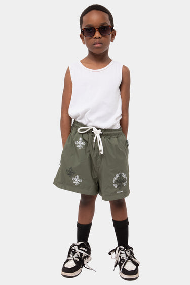 Maillot de bain enfant Jakarta Kaki porté en pied par un garçon, motifs fleur de lys, cordon blanc, lunettes noires