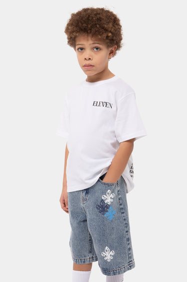 T-shirt enfant January Blanc porté de profil par un garçon, inscription Eleven noire et short en jean à fleurs de lys