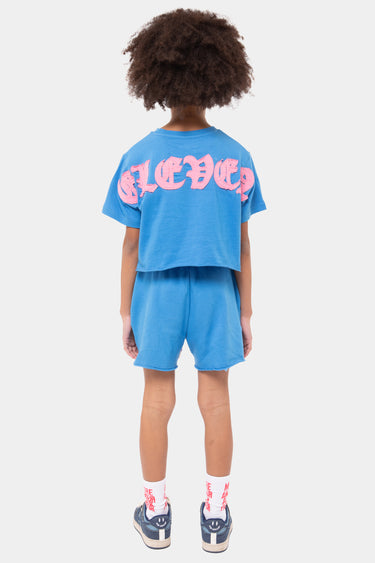 Short Julie Bleu porté par un enfant, vue de dos, uni sans motif, avec t-shirt bleu à lettres roses