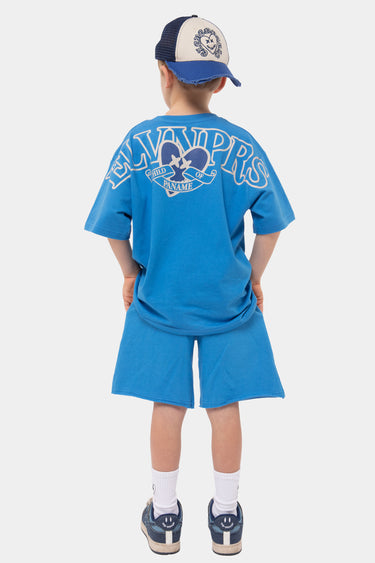 T-shirt Jude Bleu porté de dos par un enfant avec casquette, grand lettrage ELVNPRS autour d'un cœur, short bleu