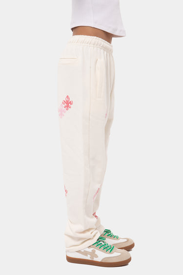 Jogging Jatacha Écru porté de profil, poche latérale et fleurs de lys roses brodées sur la jambe, baskets à lacets verts