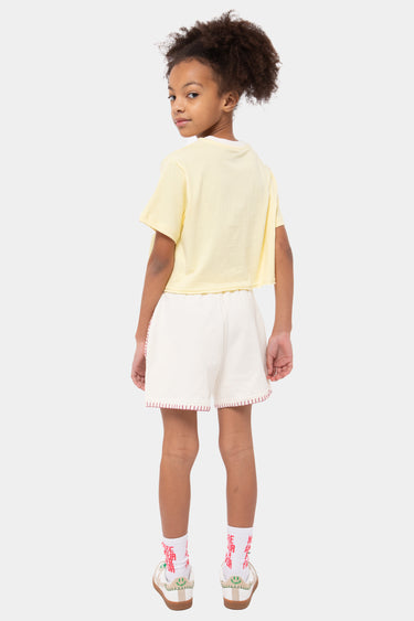 Short Poitier Écru en molleton porté par une fille de dos avec t-shirt court jaune, surpiqûres roses sur le bas, baskets