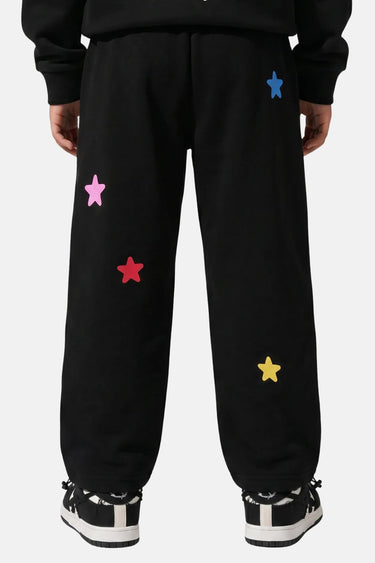 Jogging Tahar Noir porté en plan resserré, étoiles colorées appliquées sur la jambe, baskets noires et blanches