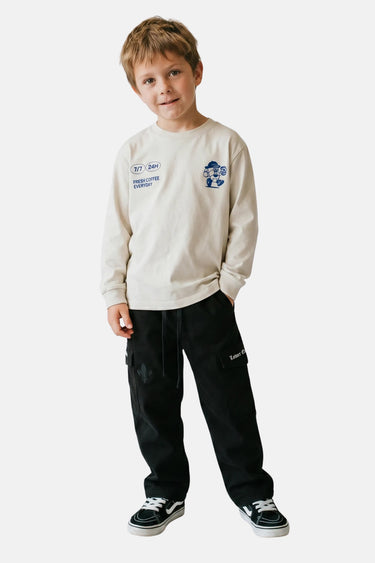 Pantalon cargo Tay Noir porté en pied par un garçon avec pull écru et baskets noires
