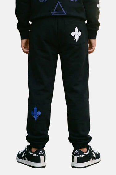 Jogging Tutti Noir porté de dos par un enfant, fleurs de lys blanche et bleue sur les jambes, baskets noires et blanches