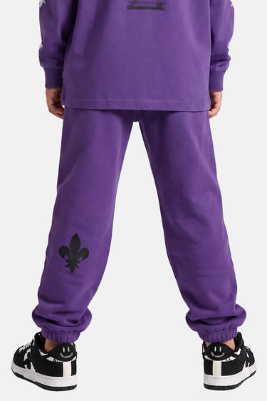Jogging Tutti Violet porté de dos par un enfant, fleur de lys noire sur le bas de jambe et baskets noires et blanches